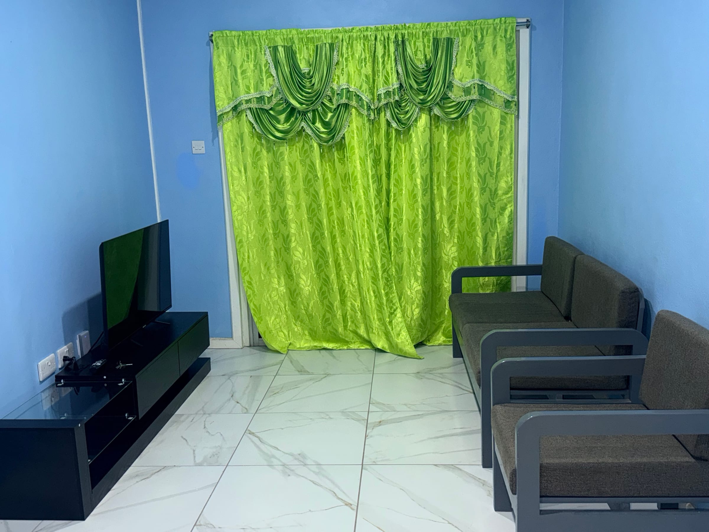 Living room with a sofa and armchair, a television on a low unit, and full-length curtains.